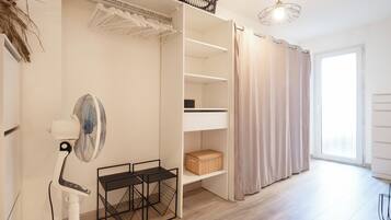 A modern room with a built-in wardrobe, a standing fan, and a window with curtains.