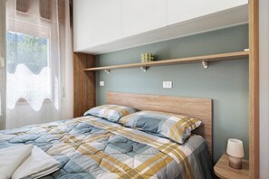 A neatly made bed with a checkered duvet, a bedside table with a lamp, and a shelf above the bed. - 'Prosecco Room' with Mountain View, Wi-Fi and Air Conditioning (Alano di Piave)