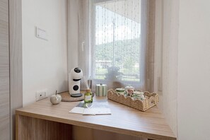 A room with a wooden desk, a window with a view of greenery, a white wall, and a power outlet.