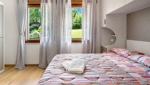 A bedroom with a bed, a window with curtains, a headboard, and a view of greenery outside.