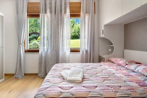 Une chambre à coucher avec un lit, une fenêtre avec des rideaux, une tête de lit et une vue sur la verdure à l’extérieur.