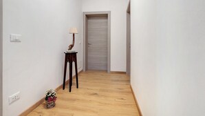 A hallway with a wooden floor, a door at the end, and a small table with a lamp and flowers.