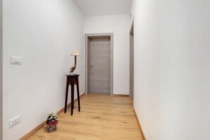 Ein schmales Gang mit Holzboden, einer geschlossenen Tür am Ende und einem kleinen Tisch mit Lampe und Blumen auf der linken Seite.