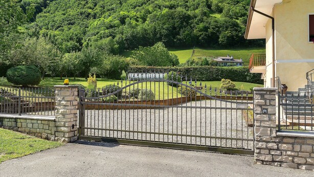 A gated property with a stone wall, a metal gate, and a view of a lush green hillside.