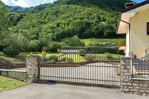 A gated property with a stone wall, a metal gate, and a view of a lush green hillside.