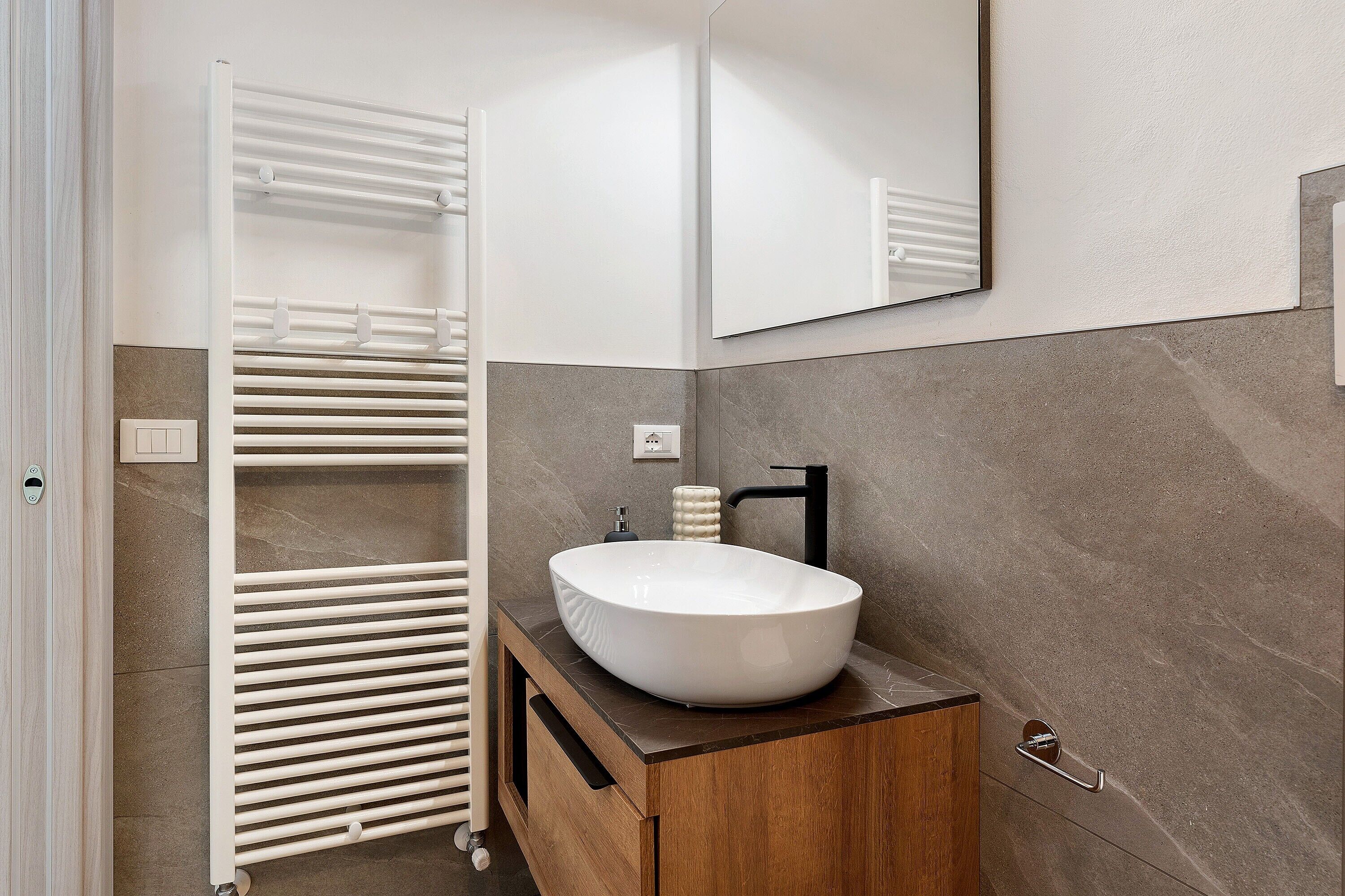 A modern bathroom with a white vessel sink, wooden vanity, and a towel rack.