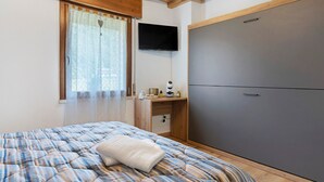 Um quarto com cama, escrivaninha, televisão e guarda-roupa.