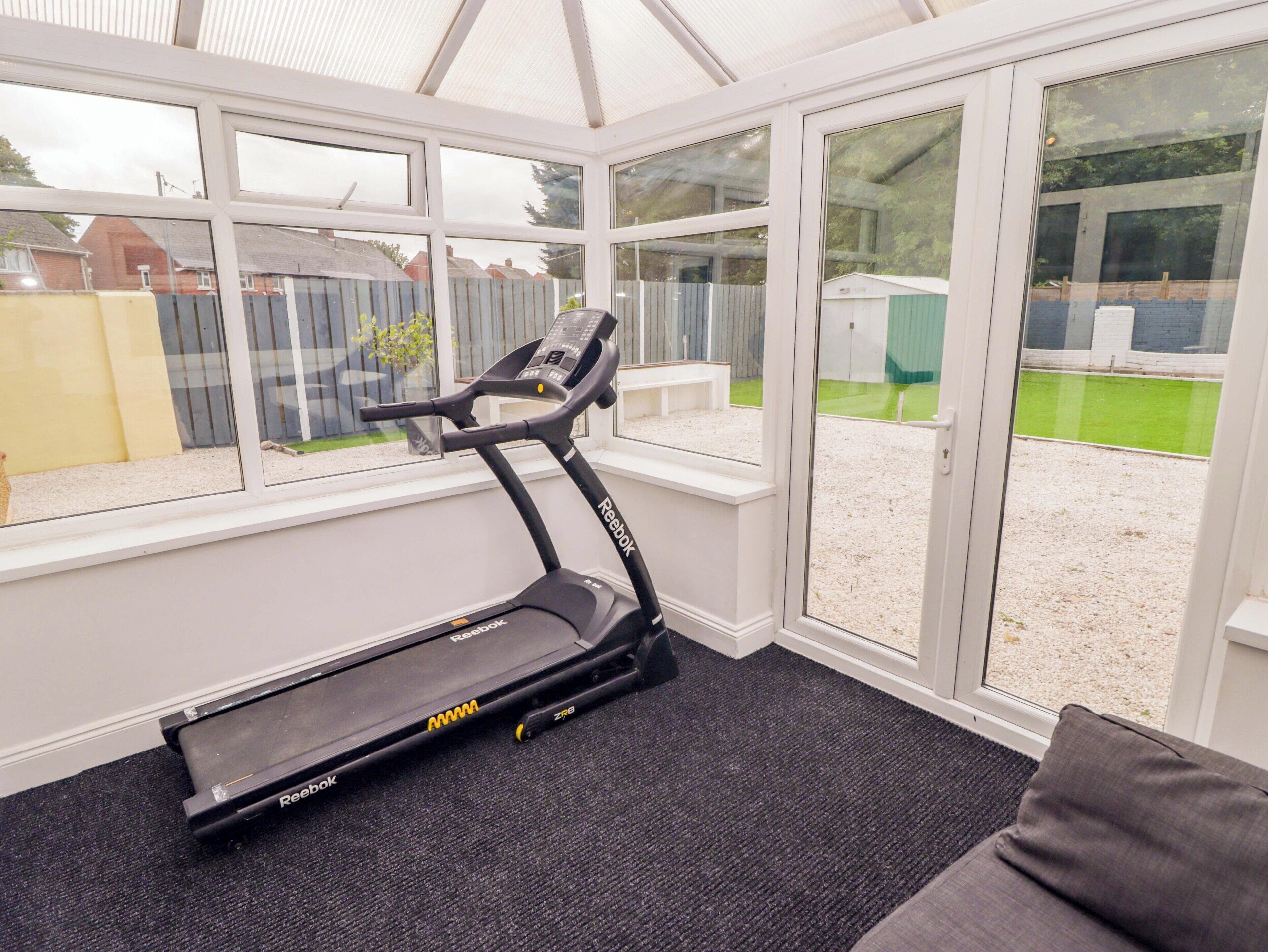 A room with a treadmill, large windows, and a view of a backyard.