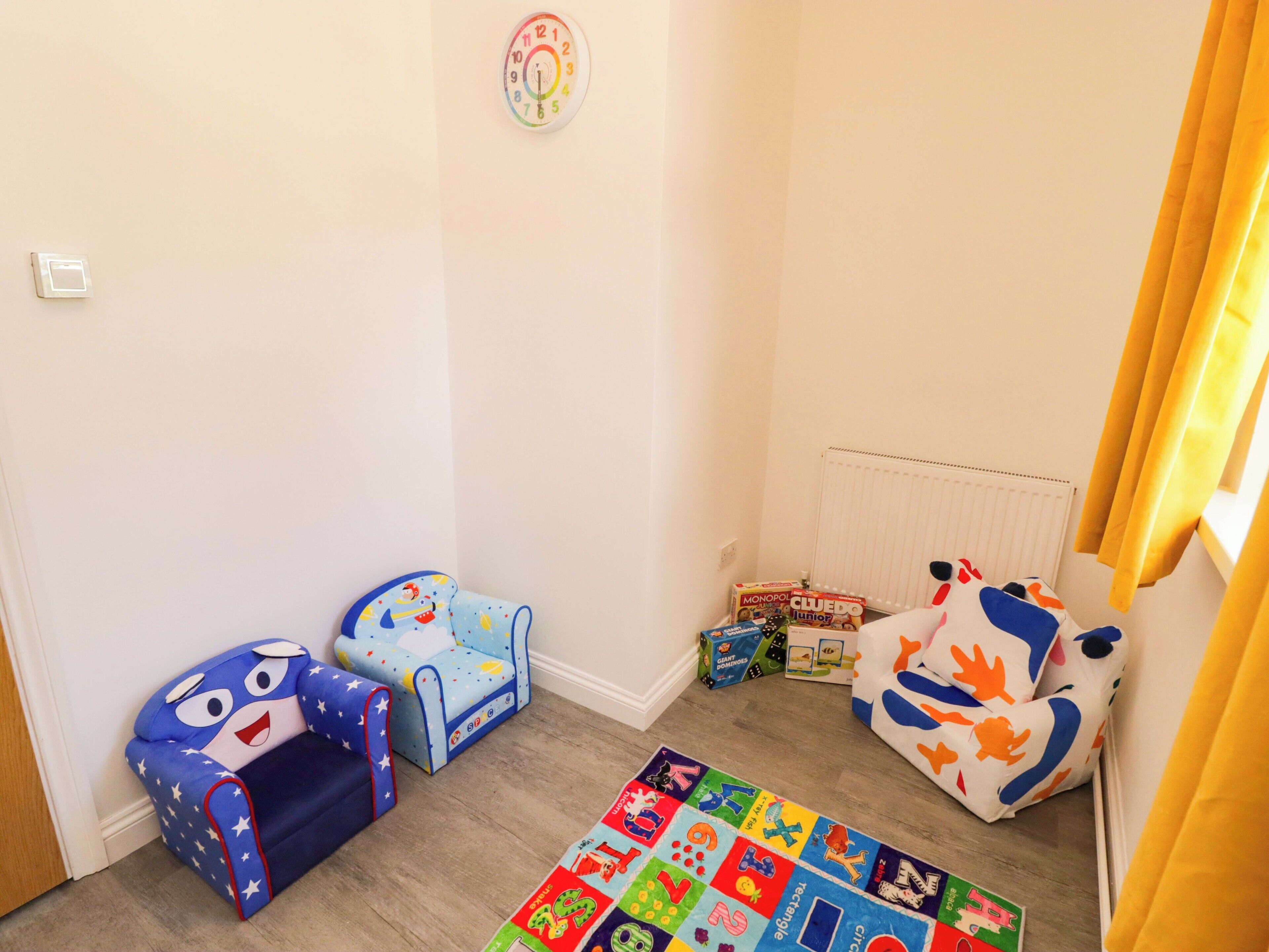 Un área de juegos para niños con un tapete de alfabeto de colores, un corral azul y blanco, y un peluche.
