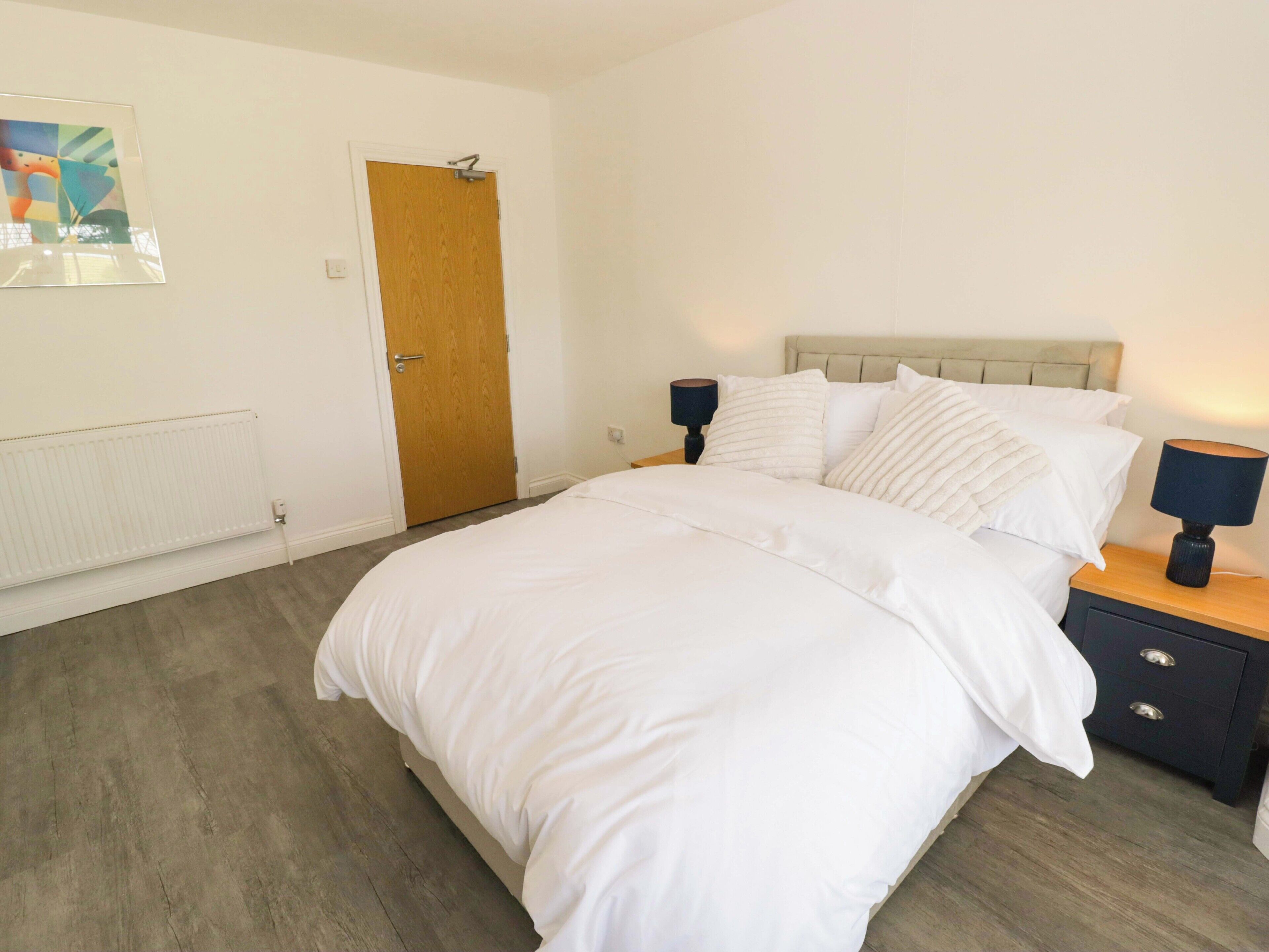Un dormitorio con cama, mesitas de noche, un radiador y una puerta.
