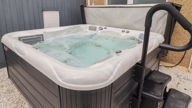 Ein Whirlpool mit schwarzem Rahmen, einer Bedienkonsole und einer weißen Abdeckung.