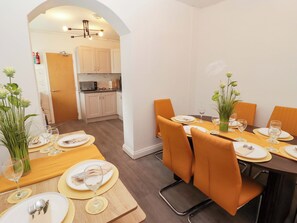 Ein Essbereich mit Tisch für vier Personen, Stühlen und einer Küche im Hintergrund.