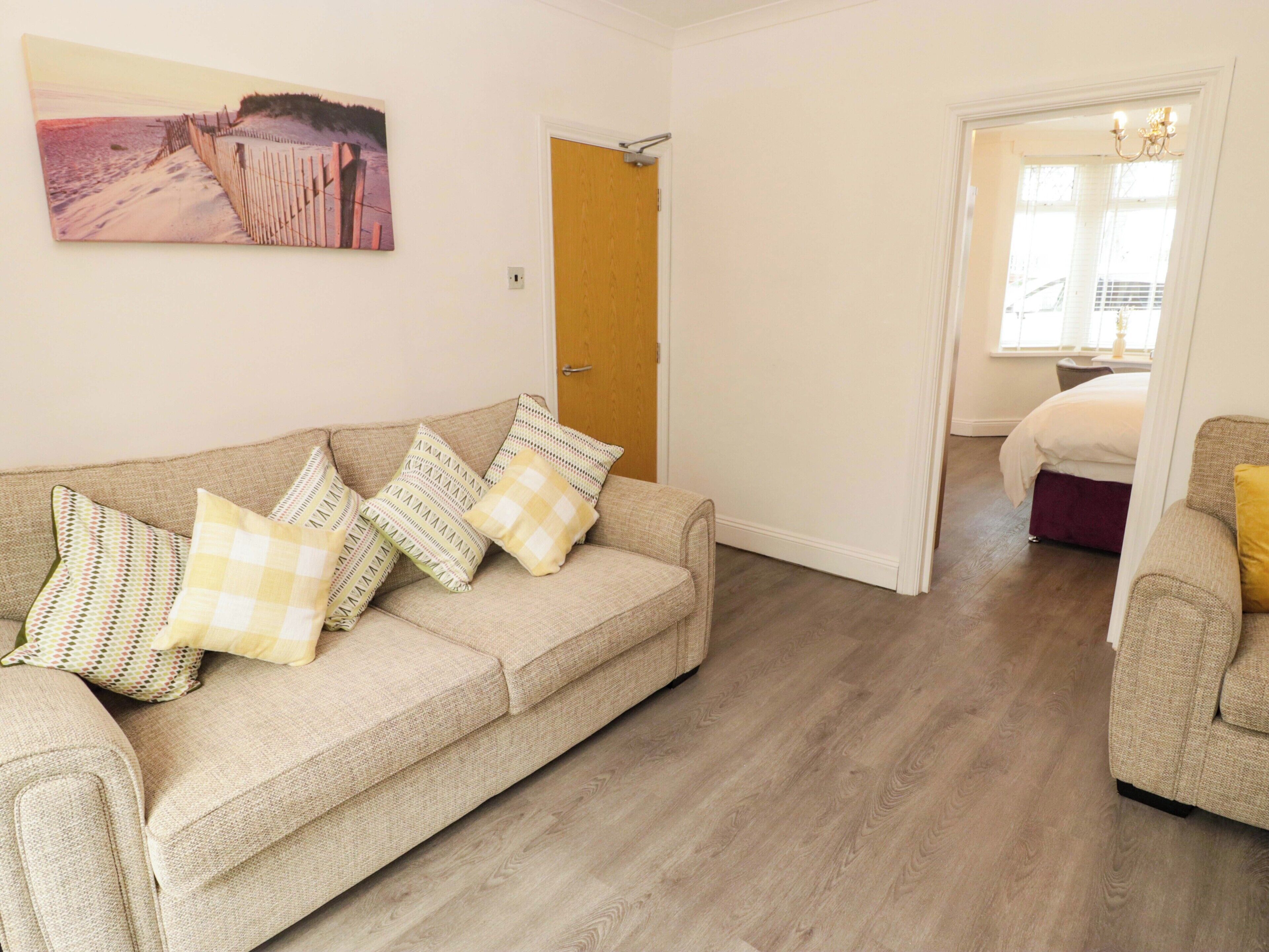 A living room with a beige sofa, patterned cushions, a wooden door, and a painting on the wall.