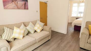 A living room with a beige sofa, patterned cushions, a wooden door, and a painting on the wall.