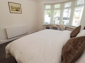 Ein Schlafzimmer mit Bett, Schreibtisch, Stuhl, Heizkörper und einem Fenster mit Jalousien.