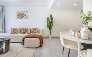 Una sala de estar moderna con sofá, reposapiés, mesa de centro y un comedor con sillas y una mesa.
