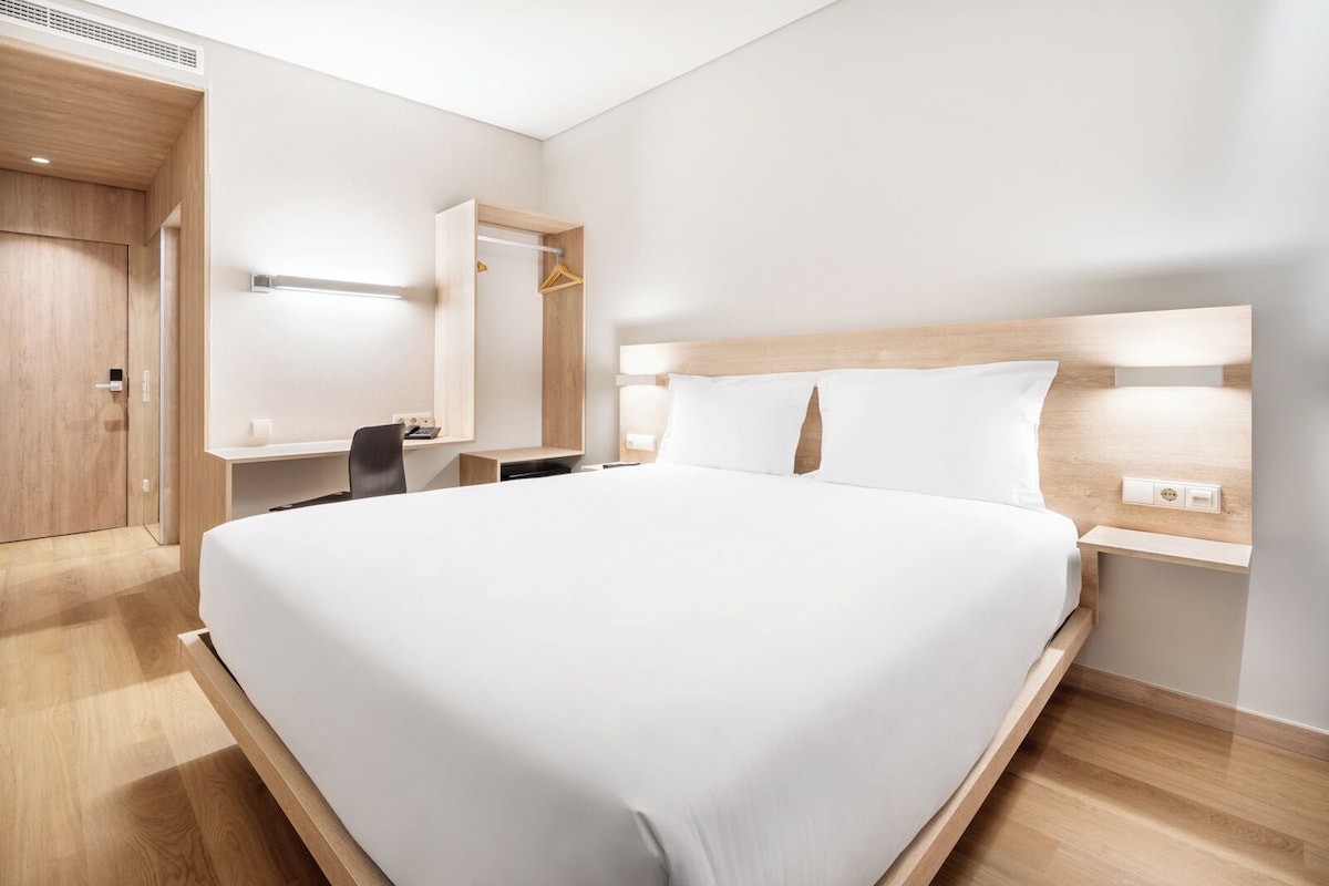 Et moderne hotelværelse med en stor seng, et skrivebord, en stol og et klædeskab.