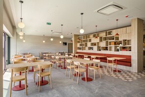 A modern cafe interior with multiple tables and chairs, a patterned floor, and a ceiling with a unique design. - Moov Hotel Matosinhos Sul (Matosinhos)