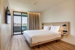 A hotel room with a large bed, a TV mounted on the wall, a balcony with a view, and a wooden floor. - Moov Hotel Matosinhos Sul (Matosinhos)