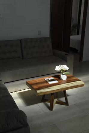 A living room with a sofa, a wooden coffee table with a vase of flowers, and a magazine. - Punto Oriente Suites (Tonalá)