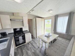 Una kitchenette compacta con estufa, horno y lavaplatos, una mesa de comedor con una silla, y un sofá.