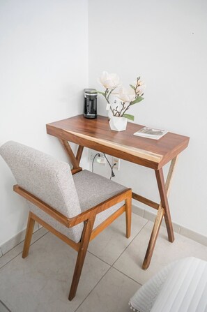 Ein kleiner Holztisch mit Stuhl, einer Blumenvase und einer Kaffeemaschine.