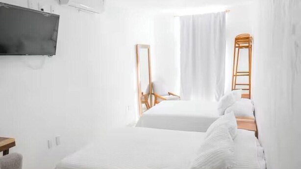 Ein Hotelzimmer mit zwei Betten, einem an der Wand montierten Fernseher, einem Sessel und einem Fenster mit Vorhängen.