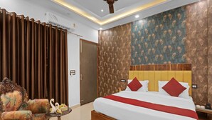 A hotel room with a bed, a sofa, a small table with a swan decoration, and a ceiling fan. - Palette The Oraya Greens (Lucknow)