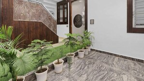 A reception area with a wooden staircase, a reception desk, and potted plants. - Palette The Oraya Greens (Lucknow)