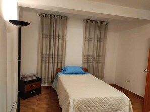 A bedroom with a bed, curtains, a bedside table, and a floor lamp. - peru in hosting (Cusco)