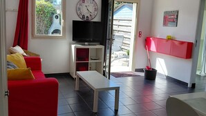 A living room with a red sofa, a white coffee table, a TV on a stand, and a window with a view of greenery. - Vacation rental near the salt marshes (Batz-sur-Mer)