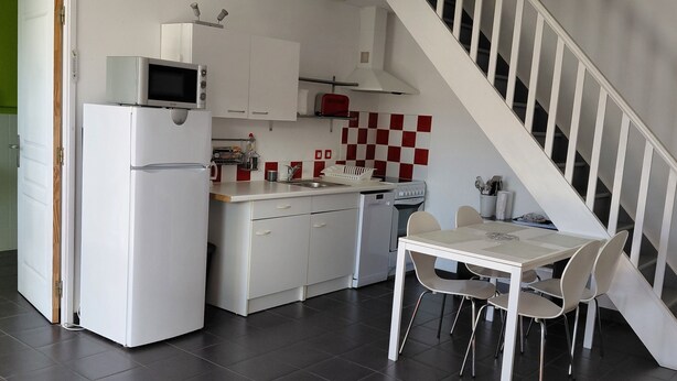 A modern kitchen with white cabinets, a microwave, and a red toaster. There's a dining area with a white table and chairs, and a staircase leading to another level. - Vacation rental near the salt marshes (Batz-sur-Mer)