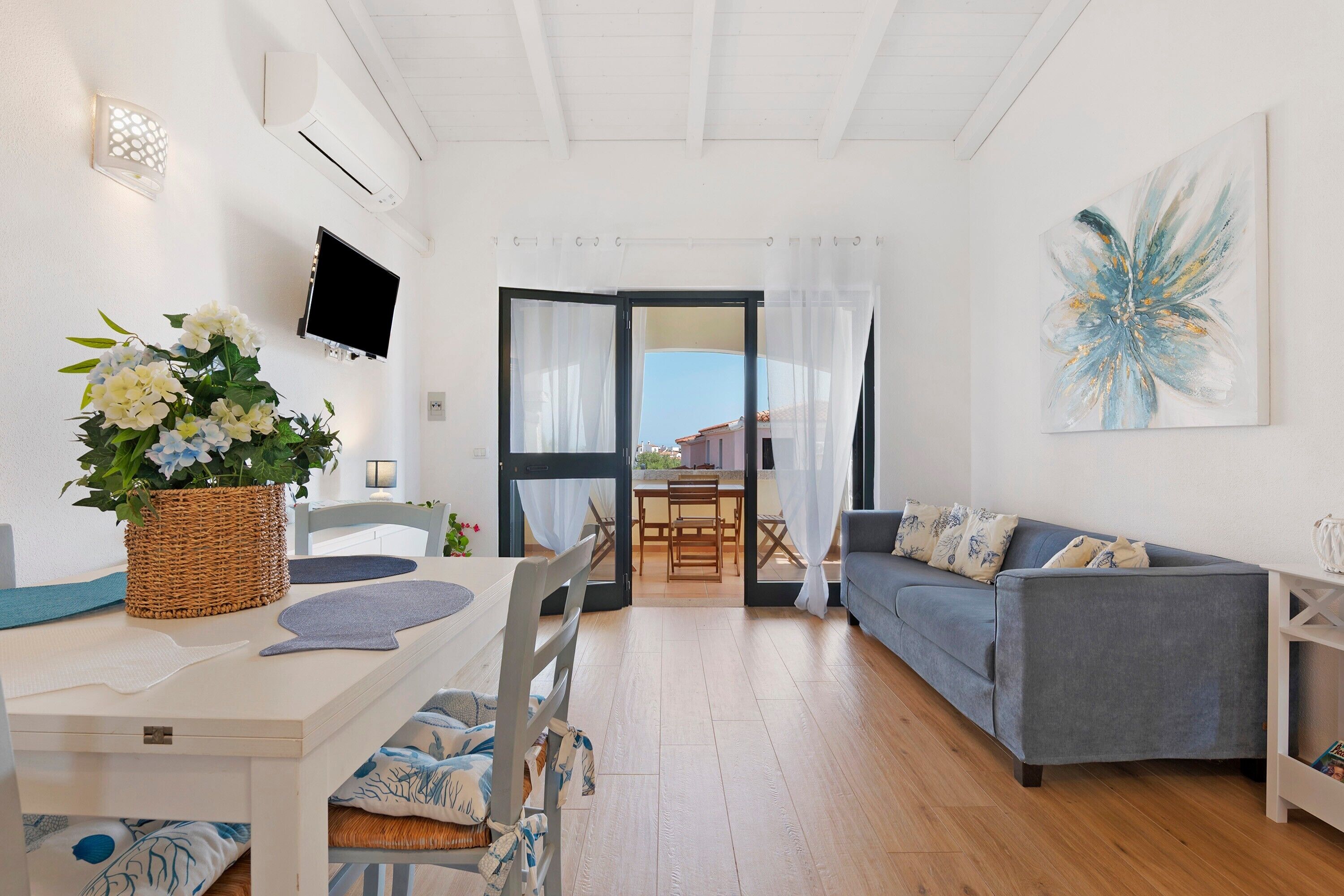 A modern living room with a sofa, dining table, and a TV mounted on the wall.