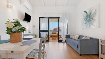 A modern living room with a sofa, dining table, and a TV mounted on the wall.