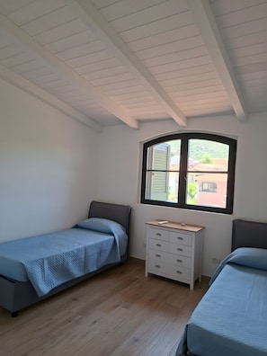 A bedroom with two single beds, a white dresser, a window with a view, and a sloped ceiling.