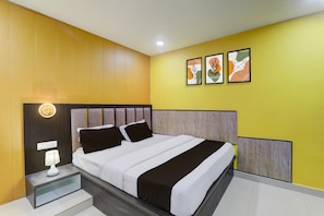 Una habitación de hotel moderna con cama, mesita de noche, lámpara y una obra de arte en la pared.