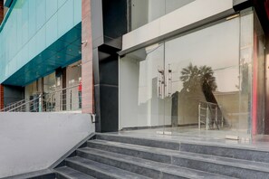 Un edificio moderno con fachada de vidrio, una escalera que lleva a una puerta y una barandilla metálica.