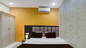A hotel room with a bed, a nightstand, an air conditioning unit, and a wardrobe. - Classic Medical College Basaratpur (Gorakhpur)