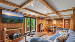 Interior acogedor de una cabaña con una televisión grande, vigas de madera, un comedor y un sofá.
