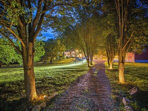 A pathway lined with trees leading to a building with illuminated windows. - Sleeps 18 | Hot Tub, Game Room & Creek (Bryson City)