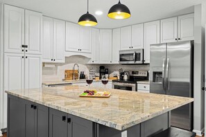 A kitchen with white cabinets, a granite countertop, stainless steel appliances, and pendant lighting. - Sleeps 18 · 7BR Estate on 6 Acres Near Bryson City — Creek, Hot Tub, Game Room (Bryson City)