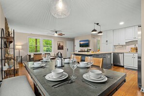 A modern kitchen with white cabinets, a dining area with a large island, and a view of greenery through the windows. - Sleeps 18 · 7BR Estate on 6 Acres Near Bryson City — Creek, Hot Tub, Game Room (Bryson City)