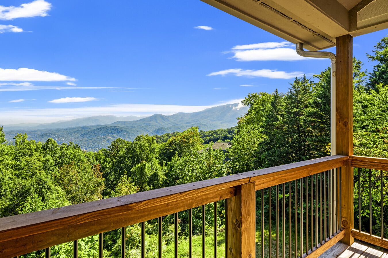 A wooden balcony with a view of a forest and distant mountains.