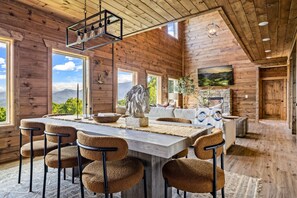 A spacious wooden cabin with a large dining table, multiple chairs, a fireplace, and a scenic mountain view. - New! Views, Sauna Spa Hottub Cantina, Dogs (Gatlinburg)