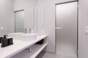 A modern bathroom with two sinks, a large mirror, and a frosted glass door. - Artisan Inspired · Strauss Boutique Studio (Vienna)