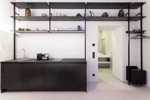 Eine moderne Küche mit schwarzem Arbeitsplatz, integriertem Spülbecken und Kaffeemaschine. Darüber befinden sich Regale mit verschiedenen Gegenständen.