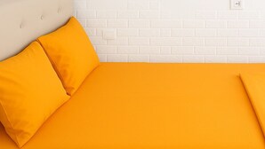 Un lit avec une tête de lit blanche et une couette orange, un mur en briques blanches et un miroir avec un cadre en bois.