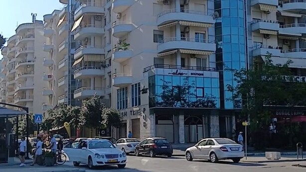 Un immeuble à plusieurs étages doté de balcons, d’une devanture de magasin et de voitures garées.