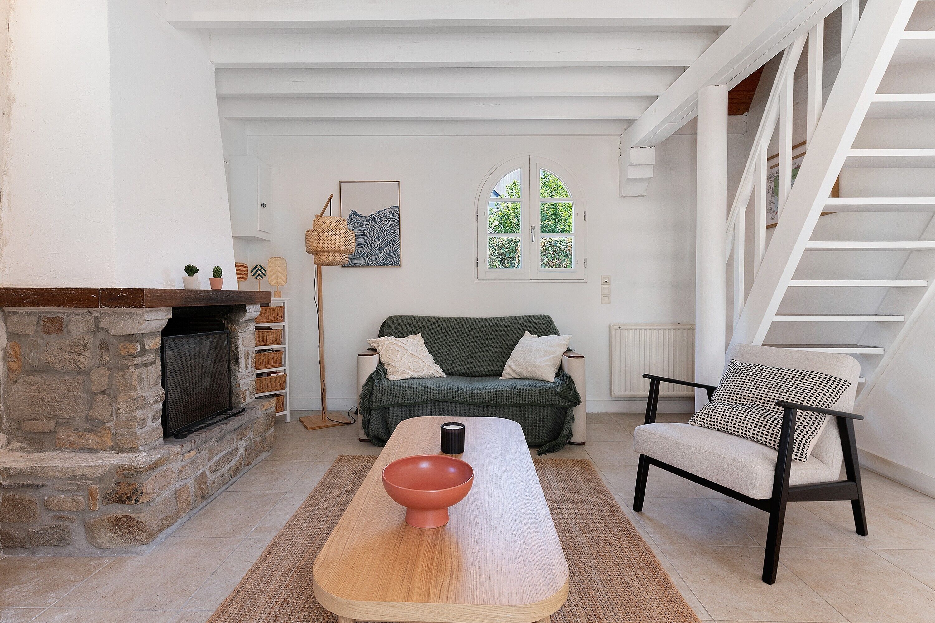 Un salon avec une cheminée en pierre, un canapé vert, une table basse en bois et un fauteuil à motifs noir et blanc.