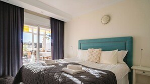 Camera d'albergo con un letto grande, una testiera color acquamarina, un comodino bianco e vista sull'esterno.
